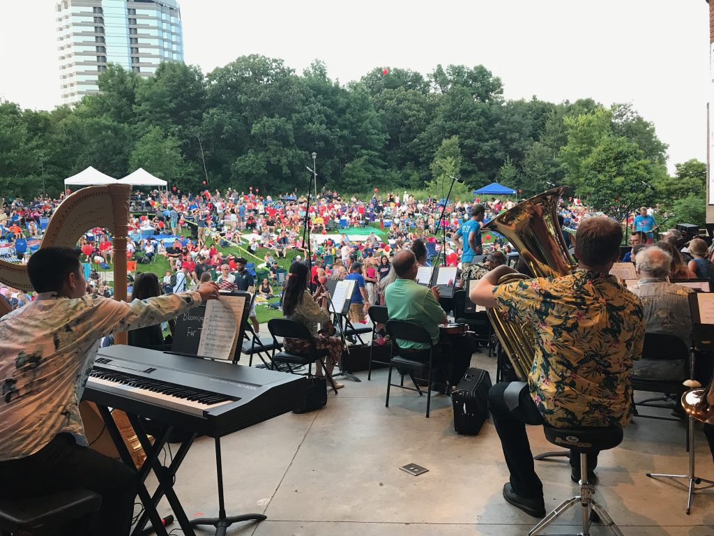 BSO musicians in colorful shirts look out at a crowd sitting on a grass lawn.