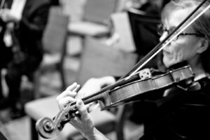 A black and white picture of a woman with glasses playing the violin, taken from the backside of the instrument.