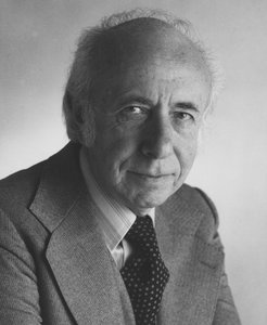 A black and white photo of an older gentleman who is wearing a suite and tie, and looking directly at the camera