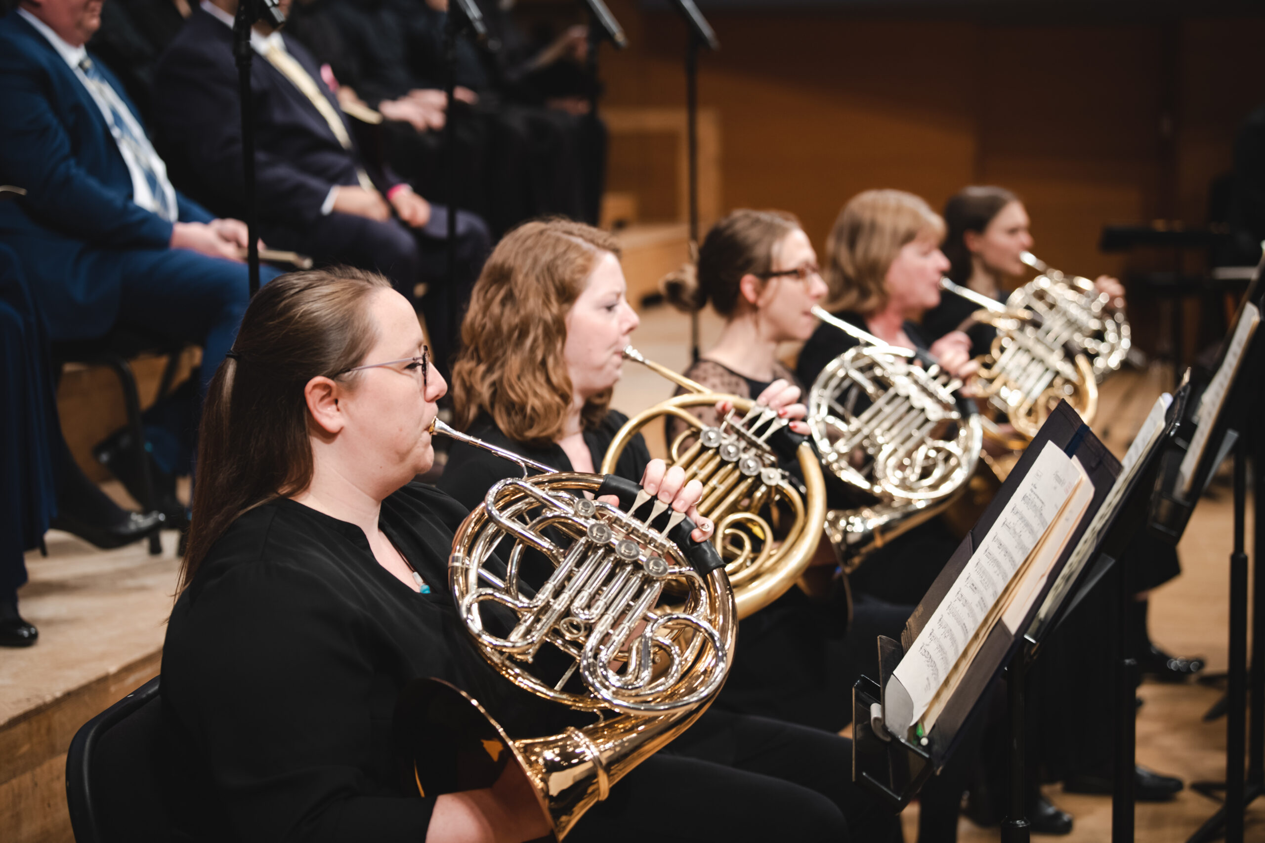 Five women, all wearing black, play five French horns