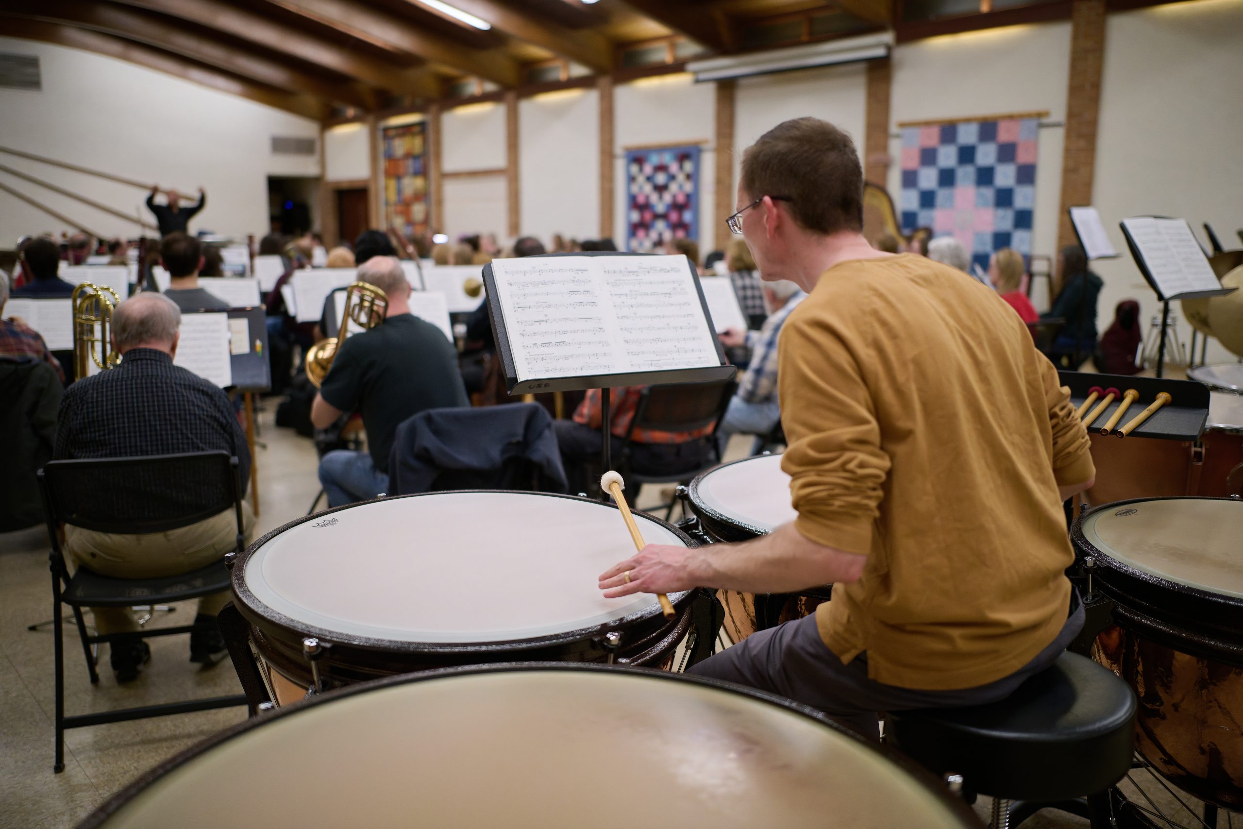 20250223-dsc_5967_54350895839_o A man in a yellow sweater plays large timpani drums.