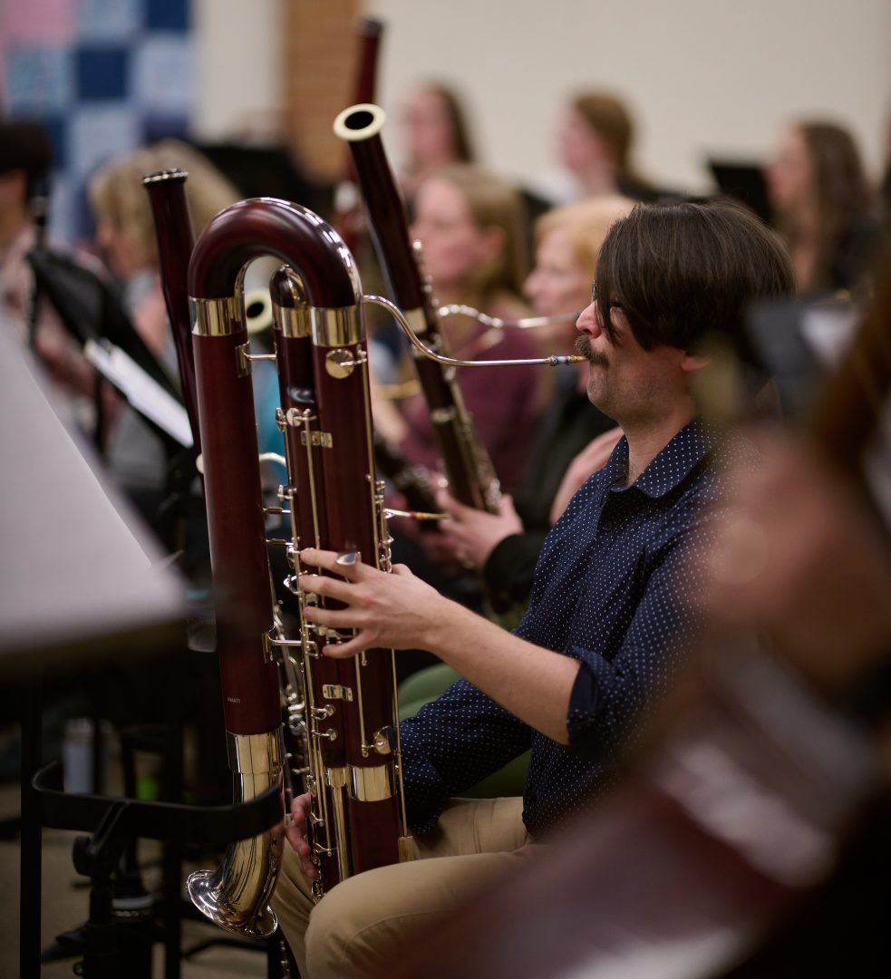 A man with dark brown hair plays a contrabassoon