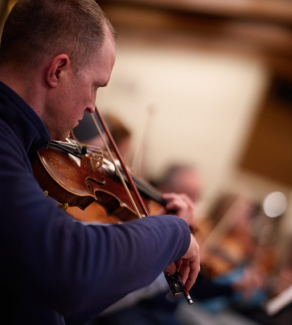 A white man in a blue shirt plays a violin
