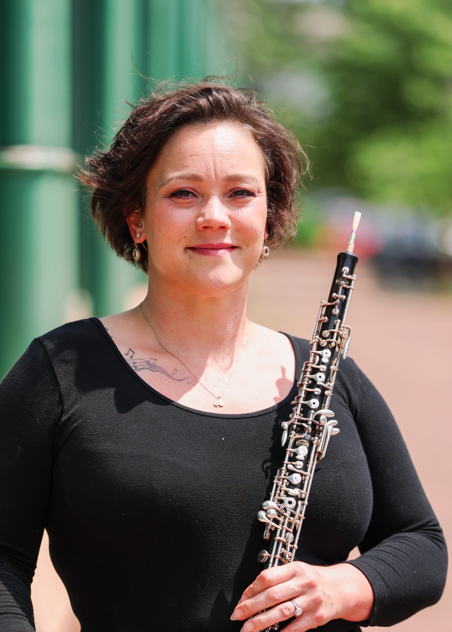 A white woman with short brown hair, wearing a black long-sleeve shirt and holds an oboe